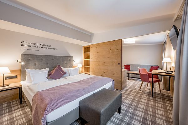 Hotelzimmer mit Doppelbett und Wohnbereich mit Couch und Schreibtisch