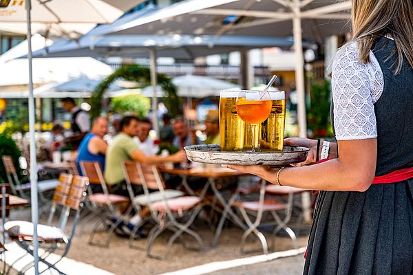 Kellnerin serviert kühle Getränke im belebten Biergarten des Ruhpoldinger Hofs
