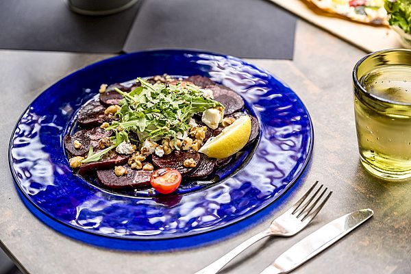 Rote-Bete-Carpaccio mit Rucola, Walnüssen und Feta auf blauem Teller mit Zitronenschnitz