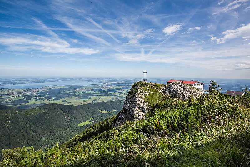 Berg mit Gipfelkreuz und Blick auf einen See im Sommer