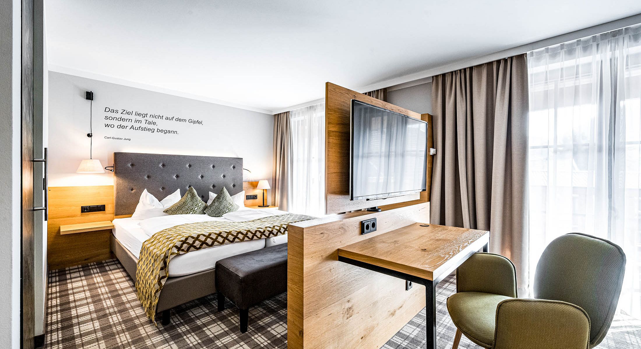 Hotelzimmer mit Doppelbett, Raumteiler und Schreibtisch mit TV
