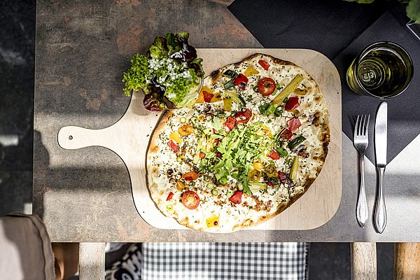 Flammkuchen mit frischem Gemüse, Rucola und Salatbeilage auf Holzbrett und gedecktem Tisch
