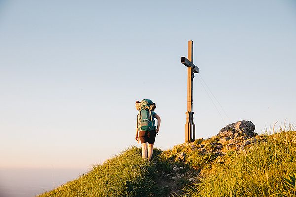 Frau mit Rucksack auf dem Weg zu einem Gipfelkreuz
