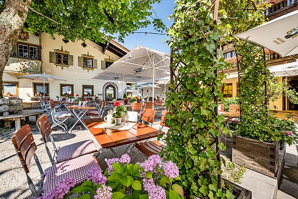Idyllischer Gastgarten mit Blumen, Sonnenschirmen und traditionellen Sitzplätzen im Ruhpoldinger Hof