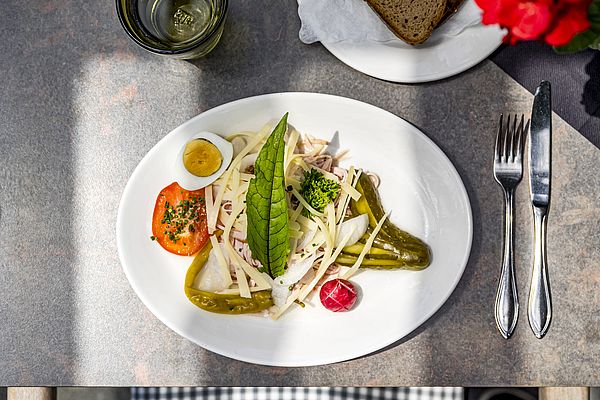 Frischer Wurstsalat mit Käse, Ei, Essiggurken und Brot auf einem gedeckten Tisch im Freien