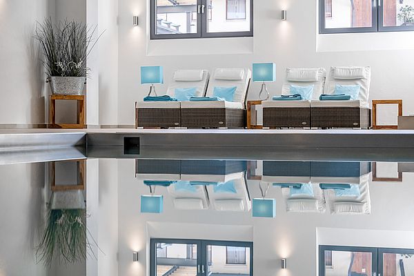 Spiegelnder Indoorpool im Wellnessbereich mit bequemen Liegeflächen